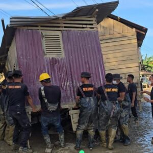 Bahu Membahu, Brimob Pindahkan Rumah Terseret Banjir yang Melintang di Jalan Nasional Tamiang–Langsa.